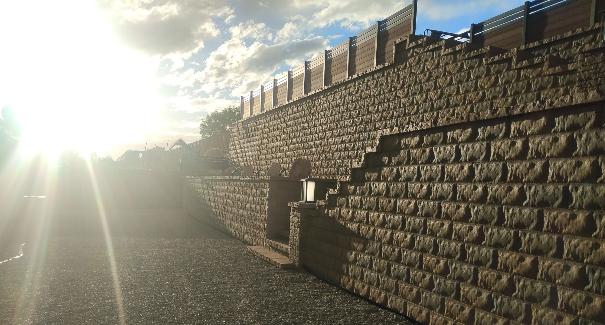 Tan block retaining wall with built-in steps and a lantern pillar by M&T’s Lawn and Yard