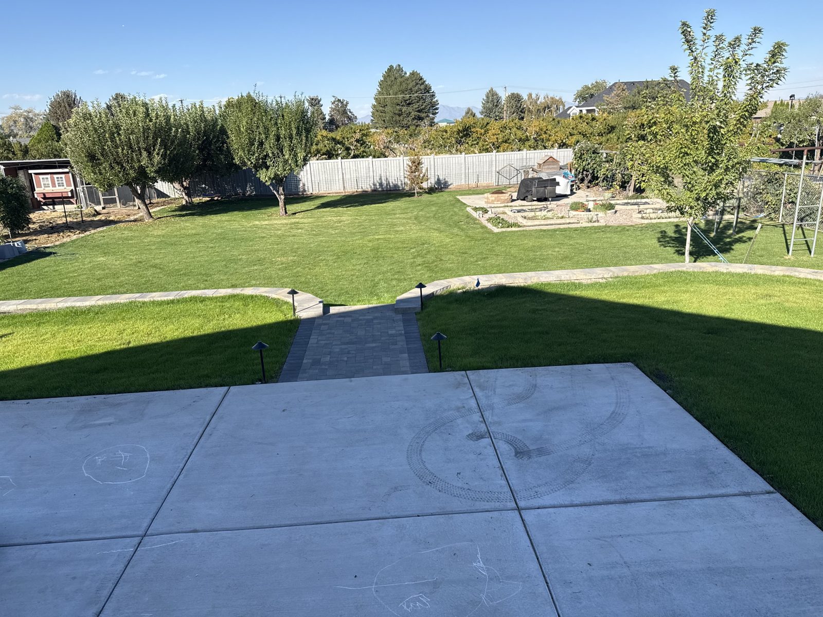 Backyard concrete patio with a paver path leading to a green lawn