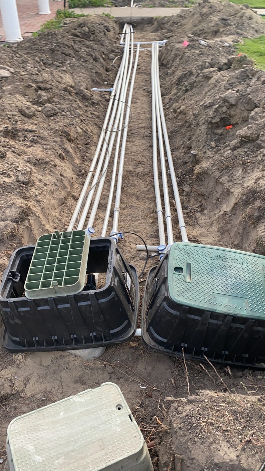 Open trench with new sprinkler main lines and valve boxes during a full system install