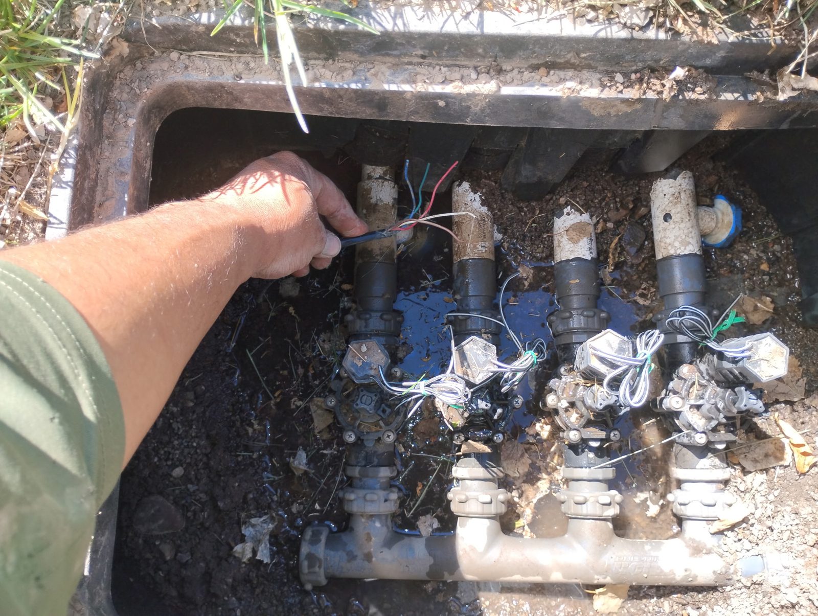 Technician repairing sprinkler valves inside a valve box