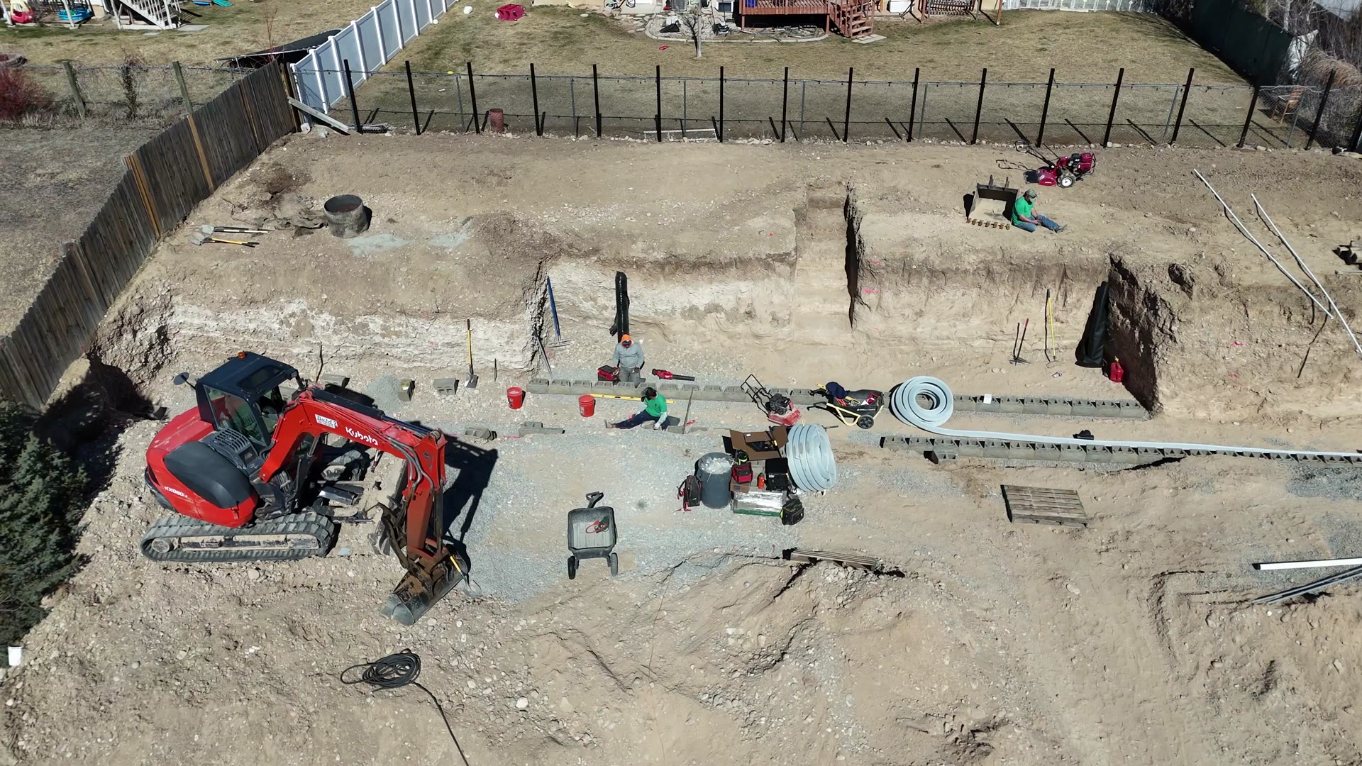 Excavator and crew setting the first course of a block retaining wall