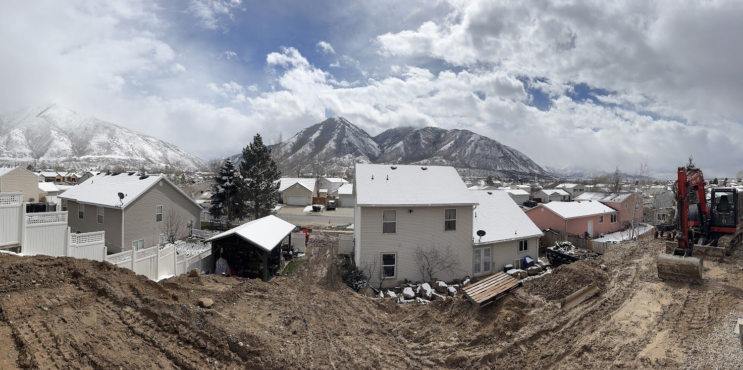 Panoramic view of the excavated backyard with excavator and mountains